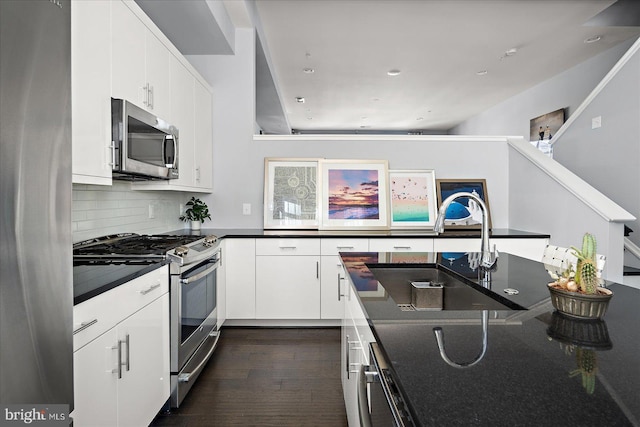 kitchen with dark wood finished floors, a sink, stainless steel appliances, white cabinetry, and backsplash