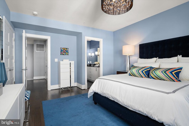 bedroom featuring baseboards, dark wood-type flooring, ensuite bathroom, and an inviting chandelier