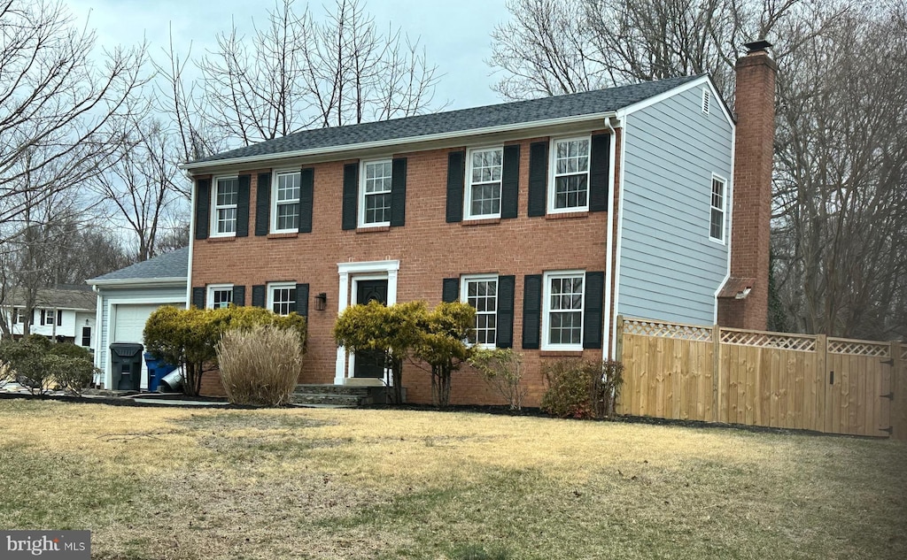 colonial inspired home featuring a garage, brick siding, fence, a front lawn, and a chimney