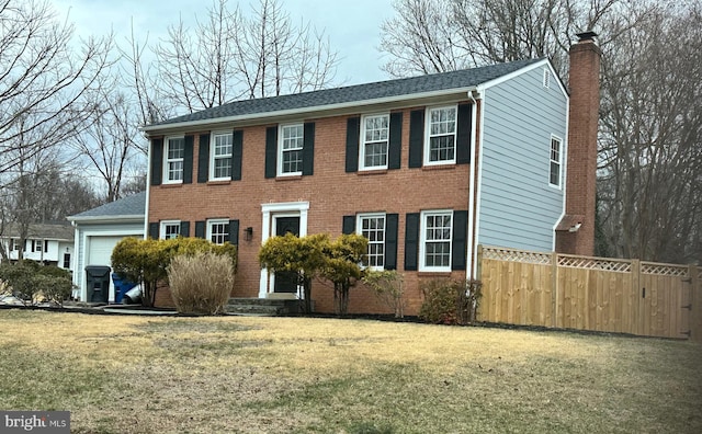 colonial inspired home featuring a garage, brick siding, fence, a front lawn, and a chimney