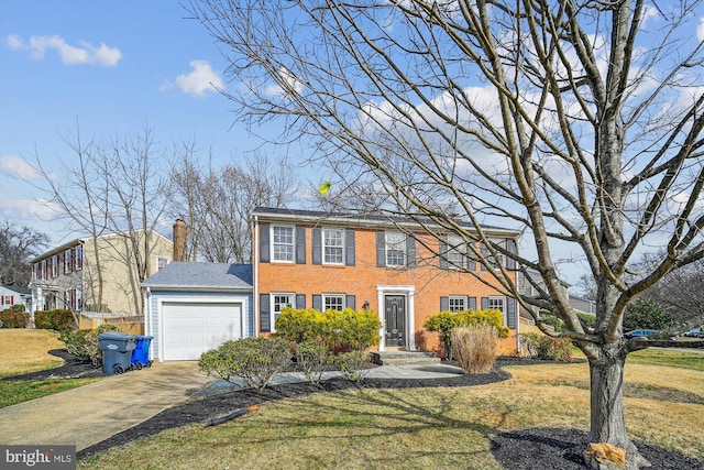 colonial inspired home featuring brick siding, concrete driveway, a front yard, a chimney, and a garage