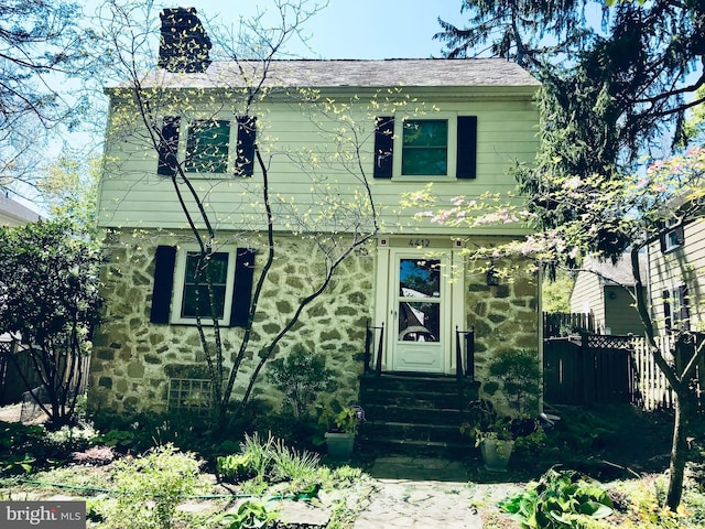 view of front of house with stone siding, a chimney, and fence