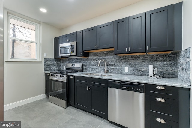 kitchen with tasteful backsplash, appliances with stainless steel finishes, light stone counters, and a sink