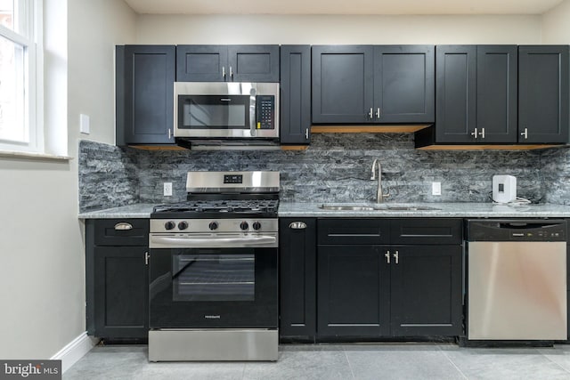 kitchen with a sink, light stone counters, tasteful backsplash, appliances with stainless steel finishes, and baseboards