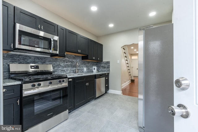 kitchen with a sink, backsplash, dark cabinetry, appliances with stainless steel finishes, and baseboards