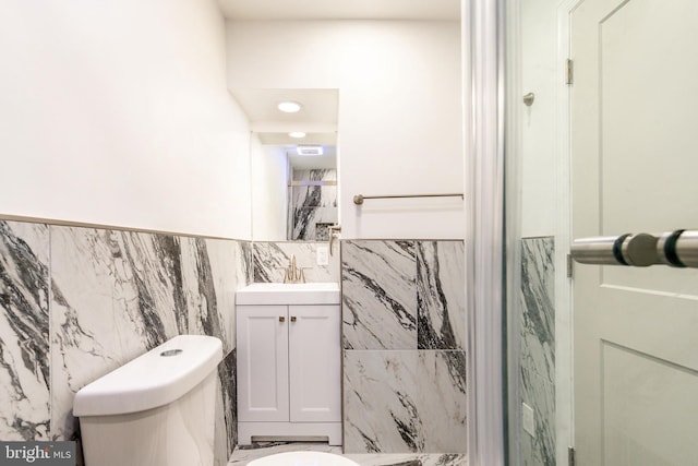 bathroom featuring vanity, tile walls, and toilet