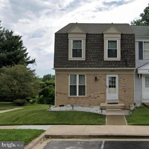 view of front of home with brick siding, uncovered parking, a front lawn, and roof with shingles