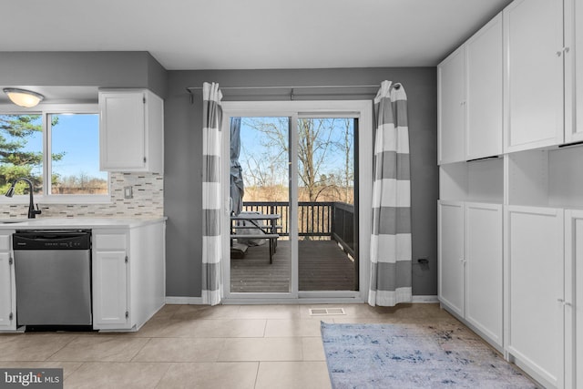 kitchen featuring visible vents, stainless steel dishwasher, white cabinets, light countertops, and decorative backsplash