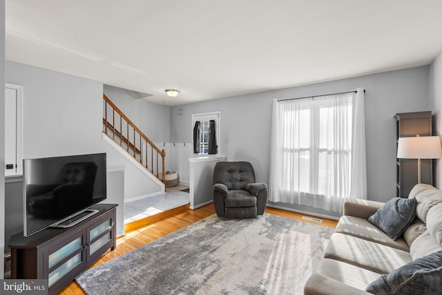 living room featuring stairway, wood finished floors, and visible vents