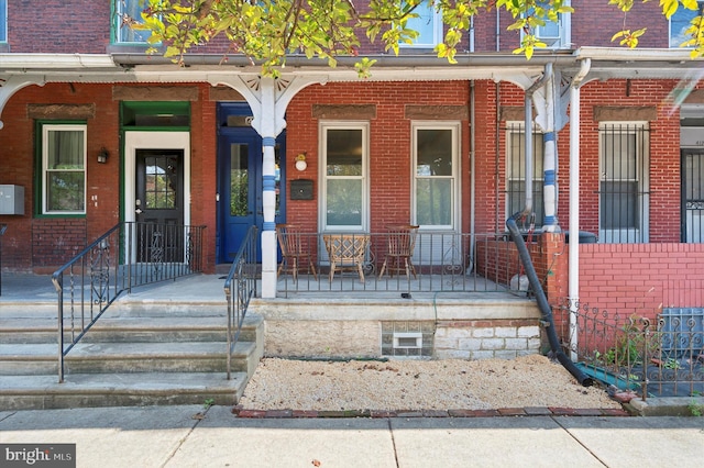 view of exterior entry with brick siding and a porch