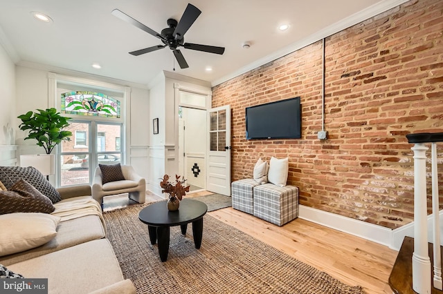 living room with brick wall, ornamental molding, and wood finished floors