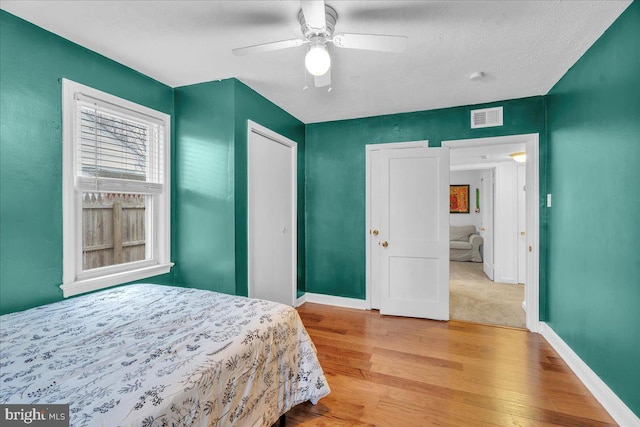 bedroom featuring a ceiling fan, wood finished floors, visible vents, and baseboards