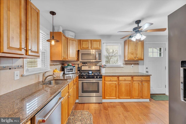 kitchen featuring stainless steel appliances, stone counters, a sink, and light wood finished floors