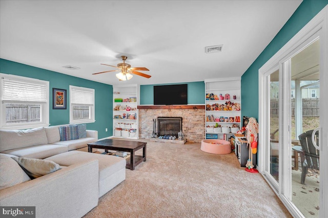 living room with a brick fireplace, built in shelves, visible vents, and carpet flooring