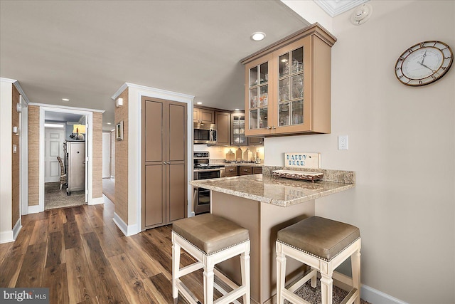 kitchen featuring glass insert cabinets, a breakfast bar area, appliances with stainless steel finishes, a peninsula, and dark wood-style floors