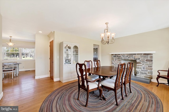 dining room with a fireplace, a notable chandelier, baseboards, and light wood-type flooring