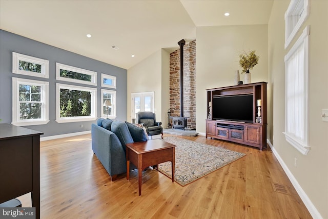 living room with a wood stove, baseboards, visible vents, and light wood-type flooring