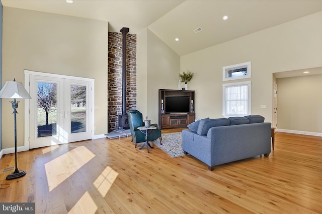 living area with visible vents, high vaulted ceiling, a wood stove, light wood-style floors, and french doors