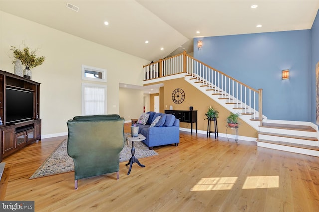 living area featuring wood finished floors, baseboards, visible vents, high vaulted ceiling, and stairs