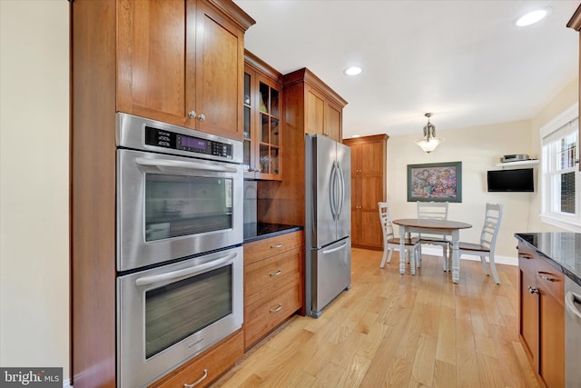 kitchen featuring brown cabinetry, light wood finished floors, appliances with stainless steel finishes, and glass insert cabinets