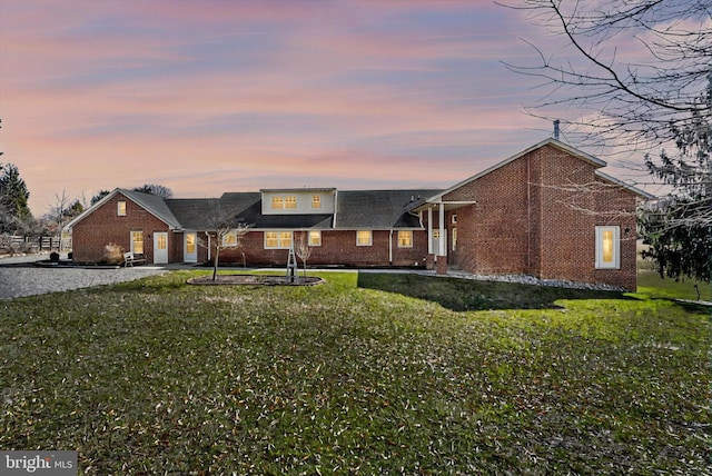 view of front of property with brick siding, driveway, and a yard