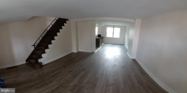 interior space featuring arched walkways, dark wood finished floors, stairway, and baseboards