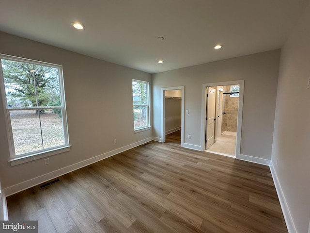 unfurnished bedroom with a walk in closet, recessed lighting, visible vents, wood finished floors, and baseboards