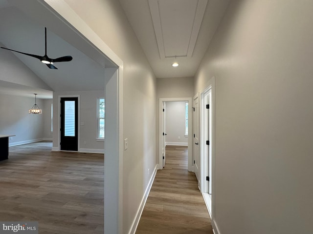 corridor featuring a chandelier, lofted ceiling, wood finished floors, baseboards, and attic access