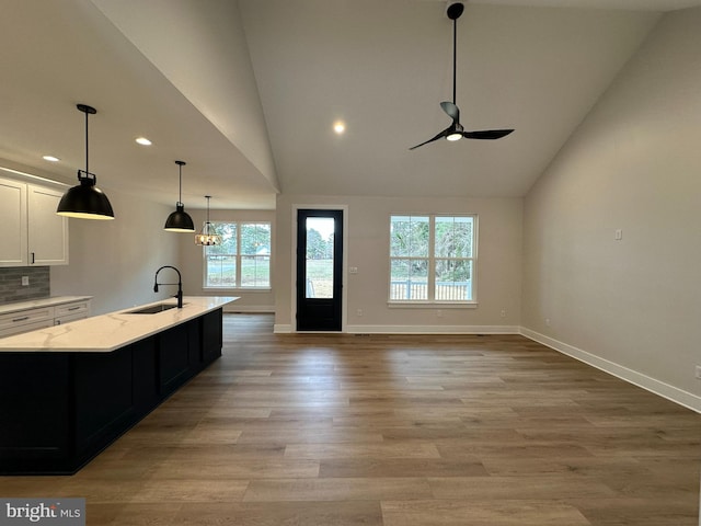 kitchen with a sink, white cabinets, light wood finished floors, an island with sink, and tasteful backsplash