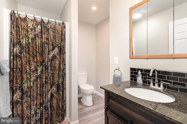 bathroom featuring tasteful backsplash, baseboards, toilet, wood finished floors, and vanity