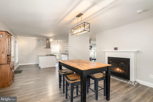 dining area featuring dark wood finished floors, a lit fireplace, and baseboards