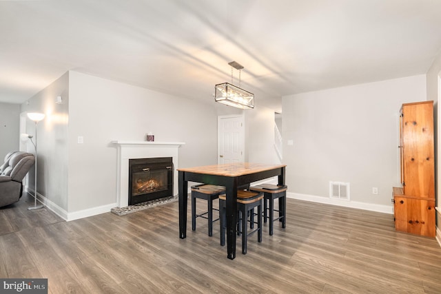 dining room with baseboards, visible vents, wood finished floors, and a glass covered fireplace