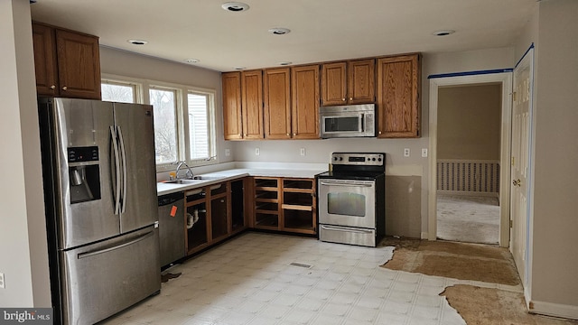 kitchen with brown cabinets, light floors, stainless steel appliances, light countertops, and a sink