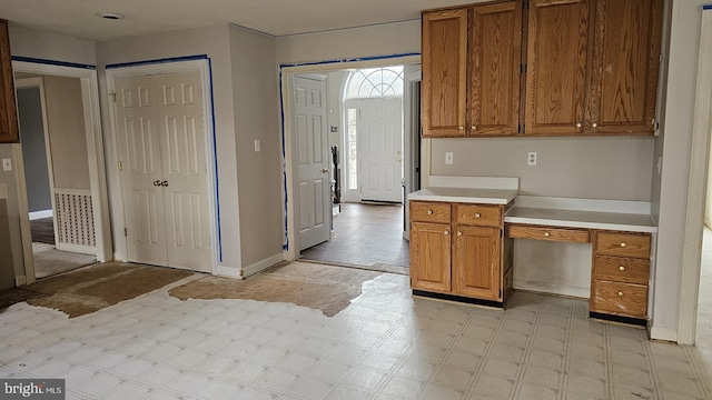 kitchen with light floors, built in desk, brown cabinetry, and light countertops