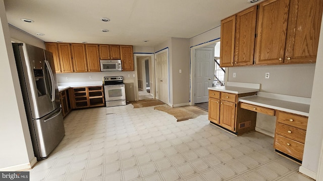 kitchen featuring stainless steel appliances, light countertops, light floors, built in desk, and brown cabinetry