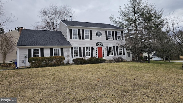 colonial inspired home with a shingled roof, a chimney, and a front lawn