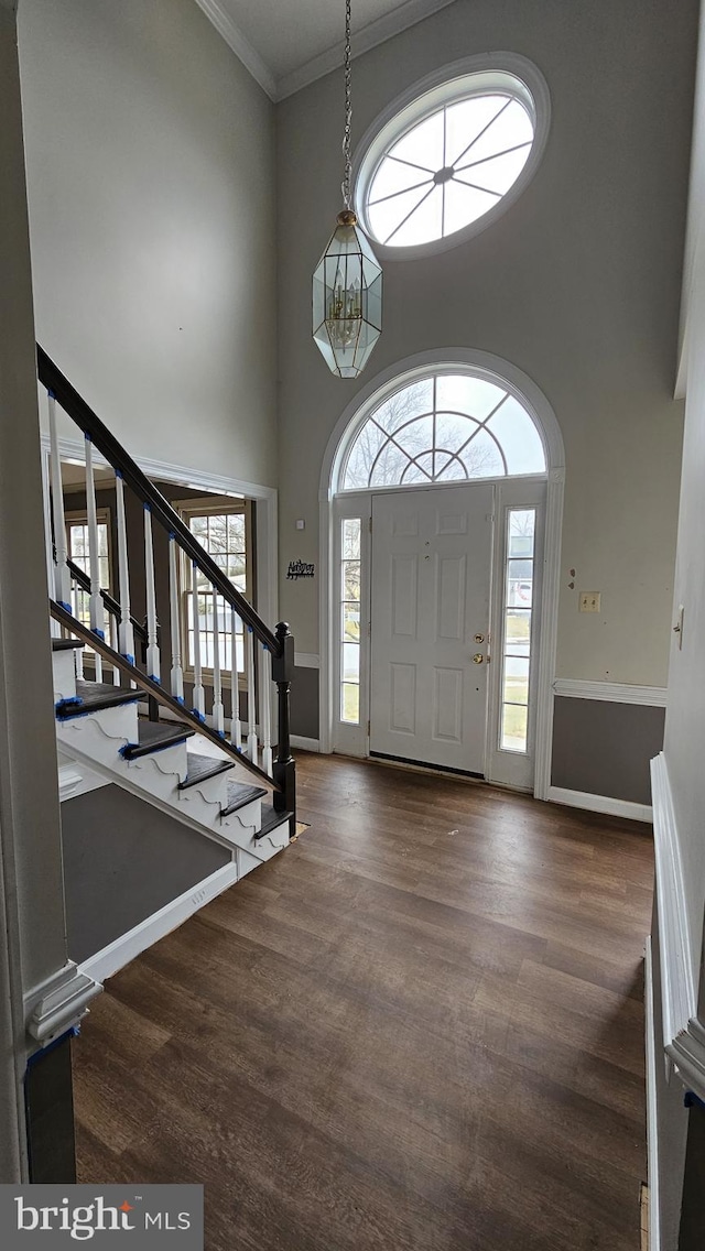 entrance foyer featuring a towering ceiling, ornamental molding, wood finished floors, baseboards, and stairs