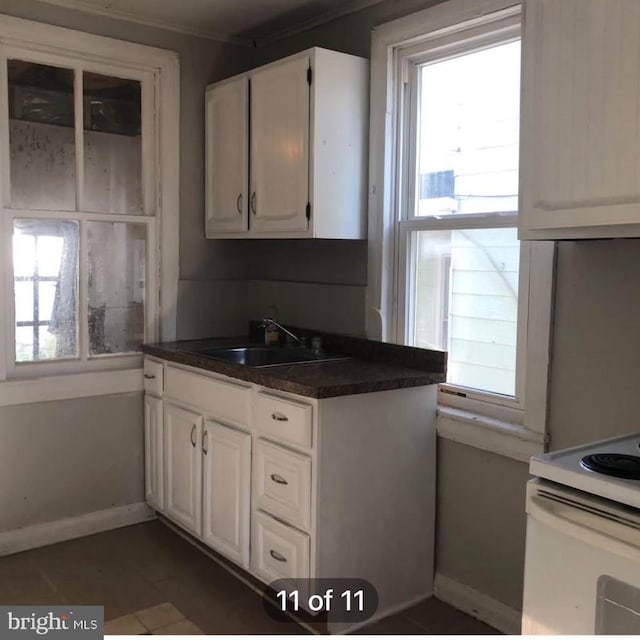 kitchen with dark countertops, a wealth of natural light, white cabinets, and a sink