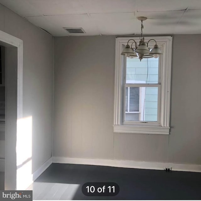 spare room with an inviting chandelier, baseboards, visible vents, and wood finished floors