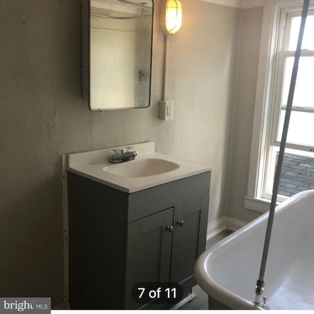 bathroom with a textured wall, a soaking tub, and vanity