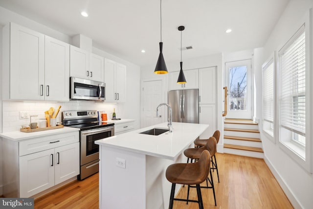 kitchen with tasteful backsplash, visible vents, a sink, stainless steel appliances, and a kitchen island with sink