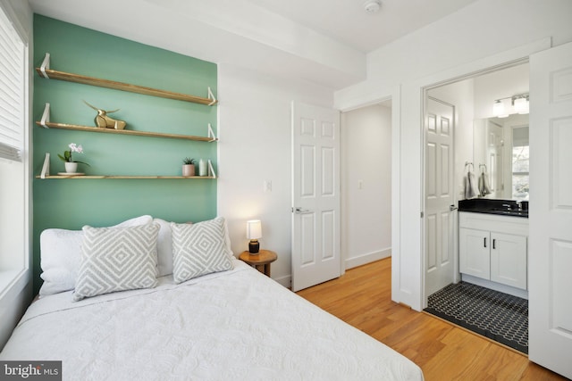 bedroom with a sink, light wood-style floors, and ensuite bath