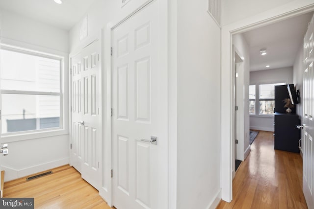 hallway with visible vents, light wood-style flooring, and baseboards