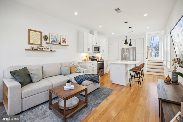 living room featuring light wood finished floors, visible vents, recessed lighting, and stairway