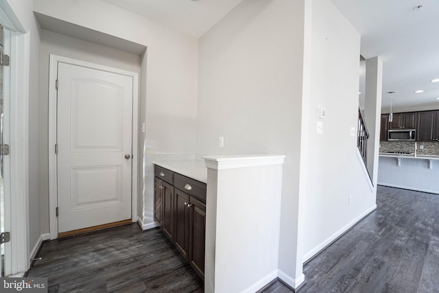 bar featuring stainless steel microwave, baseboards, dark wood-type flooring, and decorative backsplash