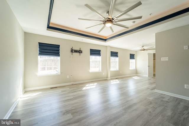 spare room with ceiling fan, baseboards, light wood-style floors, and a tray ceiling