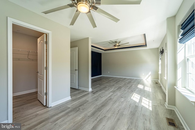 unfurnished bedroom with baseboards, visible vents, a tray ceiling, light wood-style flooring, and a walk in closet