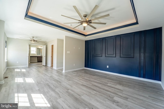 empty room with baseboards, a raised ceiling, light wood-style flooring, and a ceiling fan