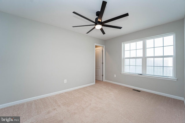 spare room featuring visible vents, light colored carpet, a ceiling fan, and baseboards