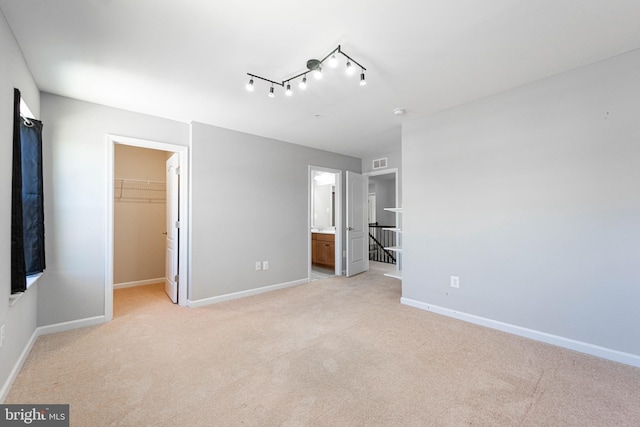 unfurnished bedroom featuring visible vents, light carpet, ensuite bath, baseboards, and a spacious closet